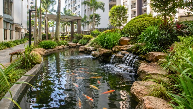 Jardim urbano de condomínio de edifícios com lago ornamental com peixes e uma cascata de pedras integrada.